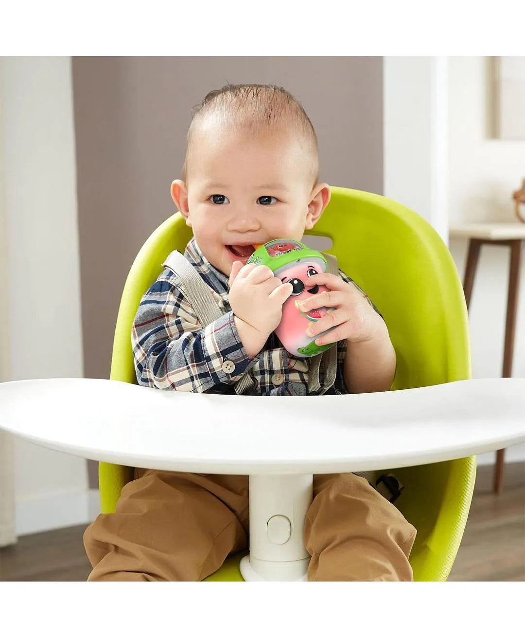 Child sitting in a green high chair holding a colorful toy indoors.